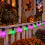Purple and green RetroGlo C9 Halloween lights strung along a porch railing
